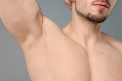 Photo of Young man showing smooth armpit after epilation procedure on light grey background, closeup