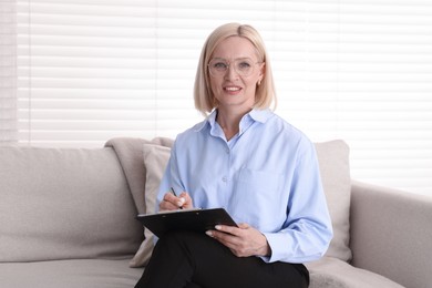 Photo of Professional psychologist with clipboard on sofa in office