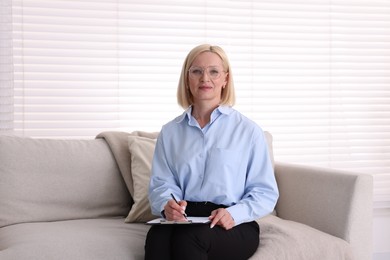 Photo of Professional psychologist with clipboard on sofa in office