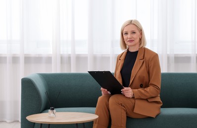 Photo of Professional psychologist with clipboard on sofa in office