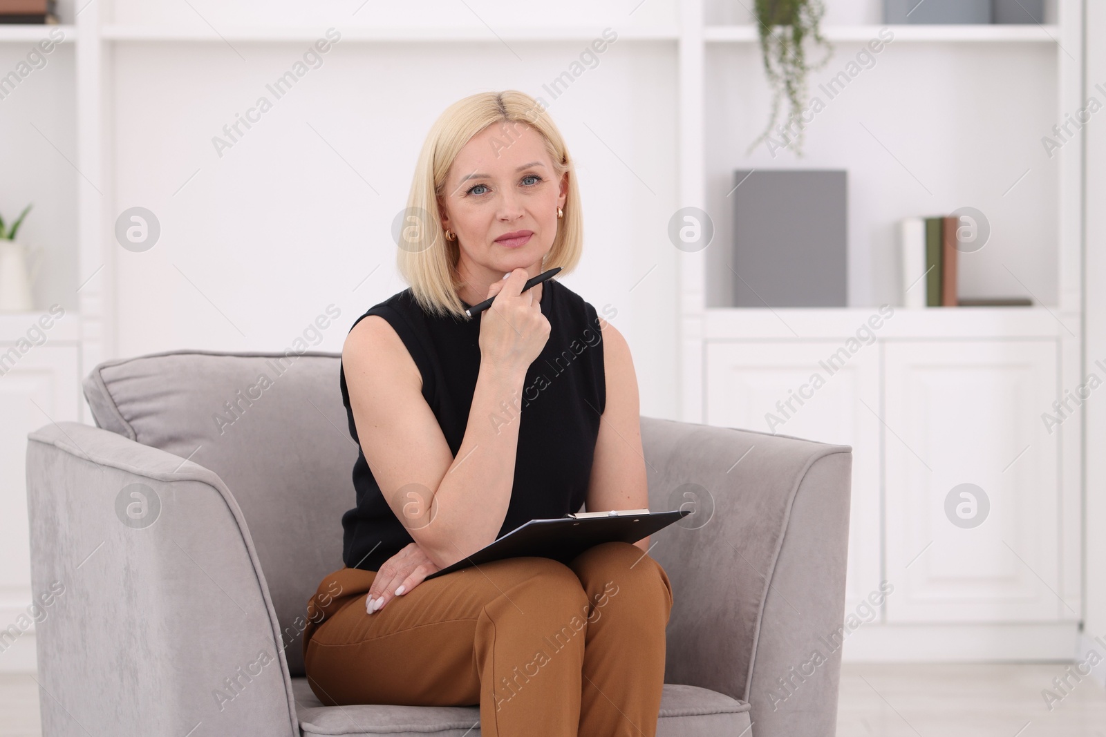 Professional psychologist with clipboard and pen in armchair indoors Photo of Professional psychologist with clipboard and pen in armchair indoors