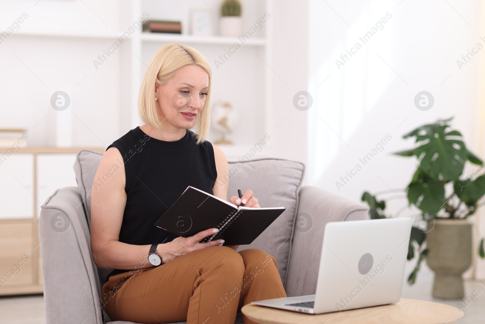 Professional psychologist taking notes while working with laptop in office Photo of Professional psychologist taking notes while working with laptop in office