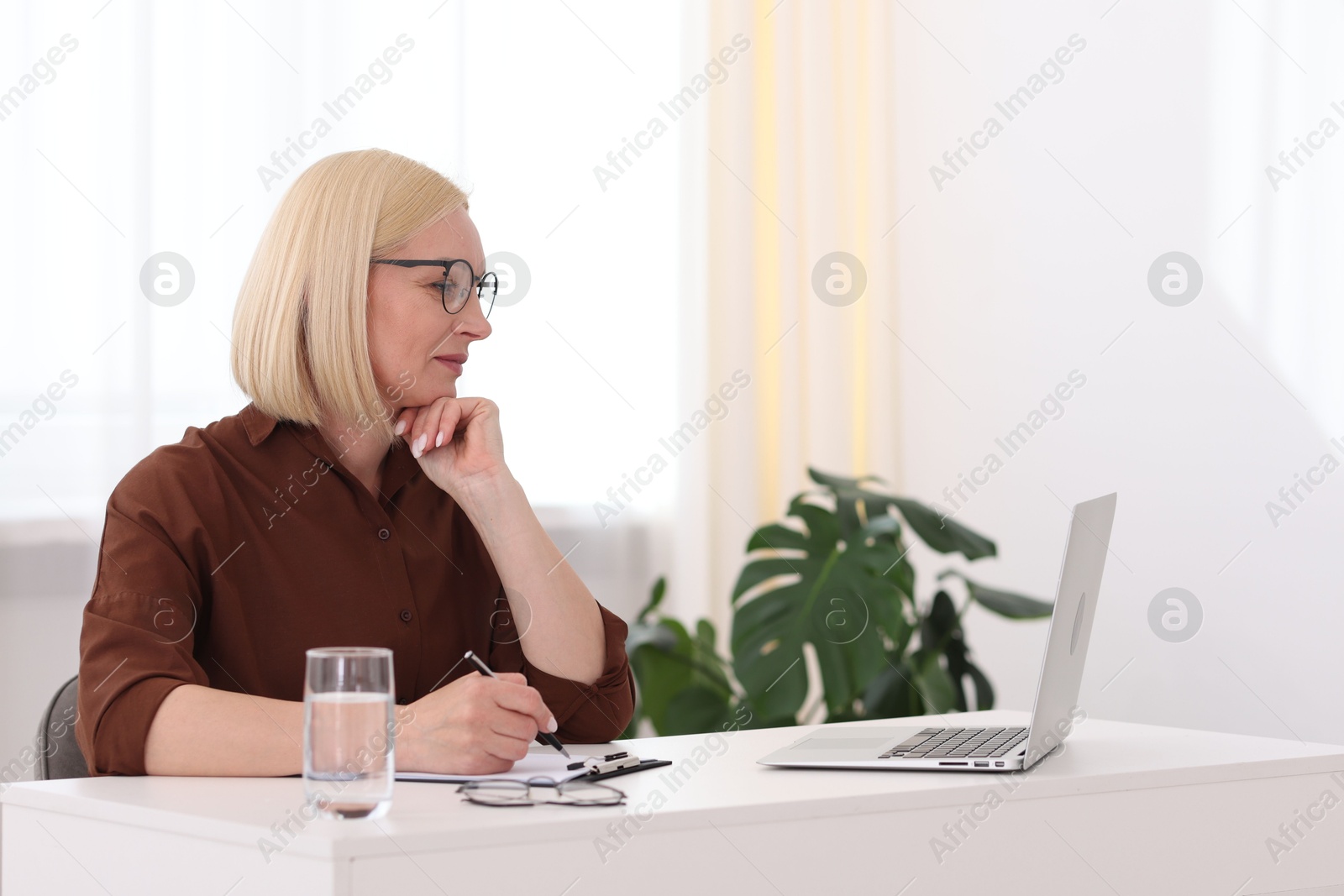 Professional psychologist taking notes while working with laptop at table in office Photo of Professional psychologist taking notes while working with laptop at table in office