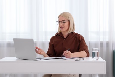 Photo of Professional psychologist taking notes while working with laptop at table in office