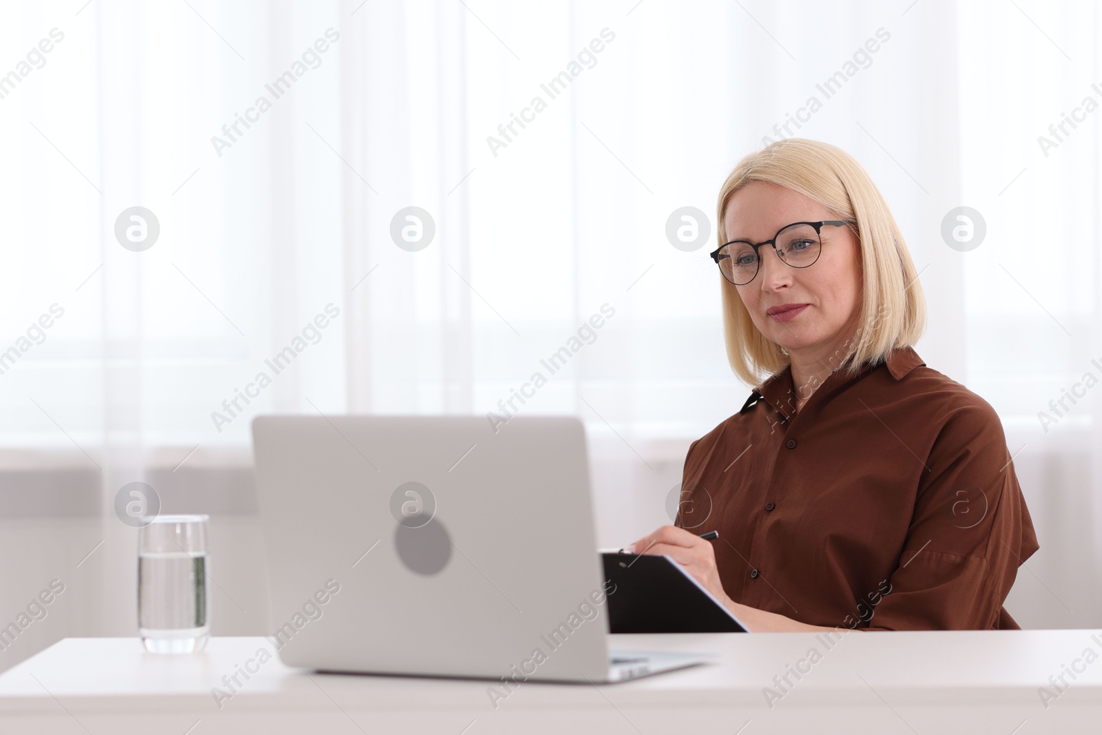 Professional psychologist taking notes while working with laptop at table in office Photo of Professional psychologist taking notes while working with laptop at table in office