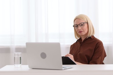Photo of Professional psychologist taking notes while working with laptop at table in office
