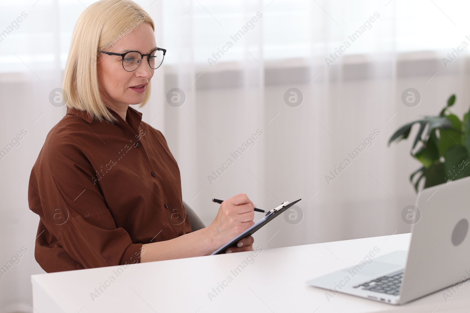 Photo of Professional psychologist taking notes while working with laptop at table in office