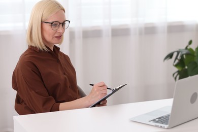 Photo of Professional psychologist taking notes while working with laptop at table in office