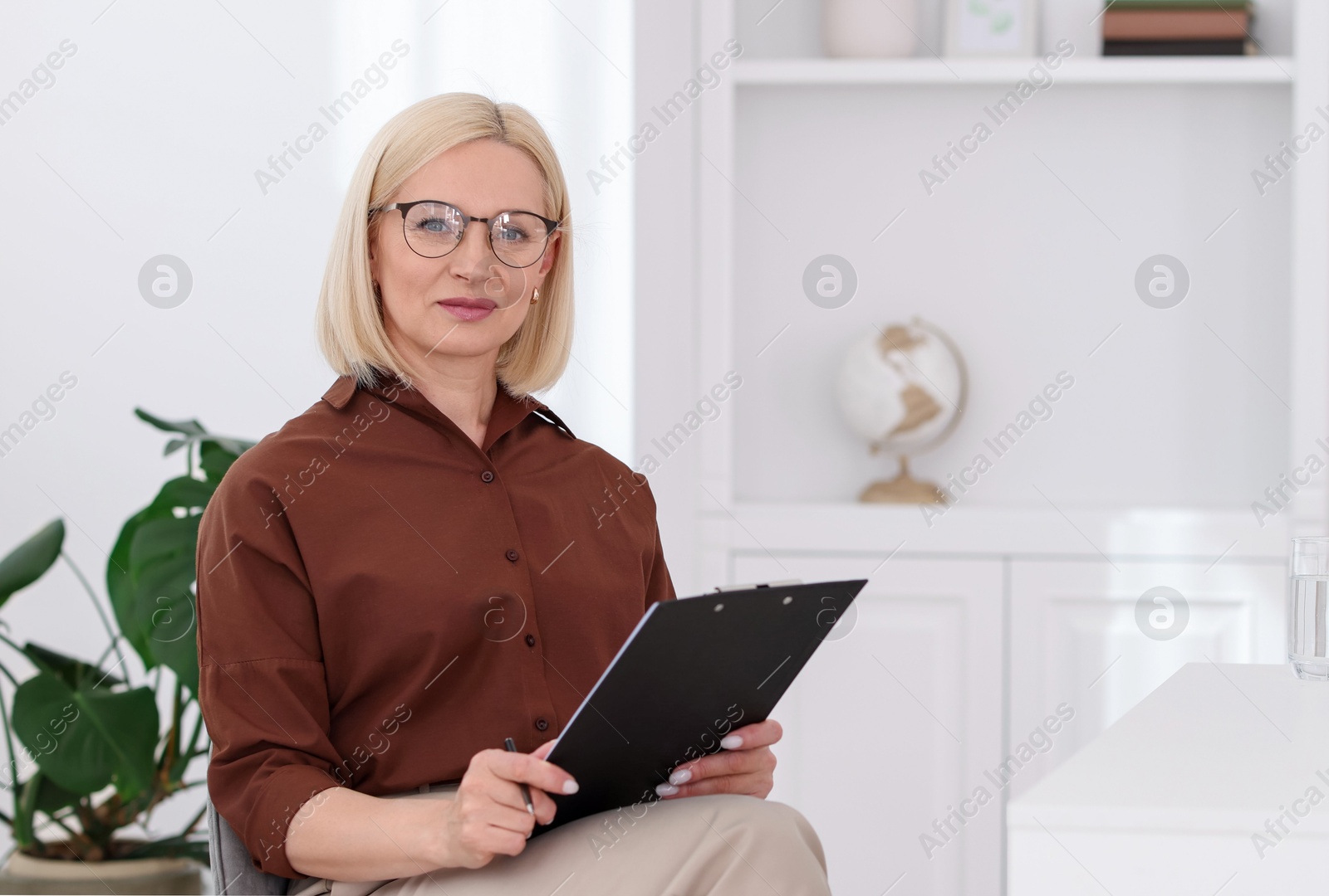 Professional psychologist with clipboard at table in office Photo of Professional psychologist with clipboard at table in office