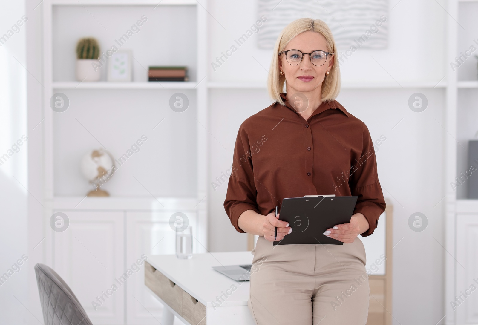 Professional psychologist with clipboard near table in office, space for text Photo of Professional psychologist with clipboard near table in office, space for text