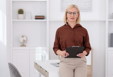 Photo of Professional psychologist with clipboard near table in office, space for text