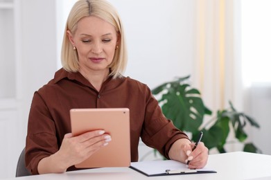 Photo of Professional psychologist with tablet taking notes at table in office