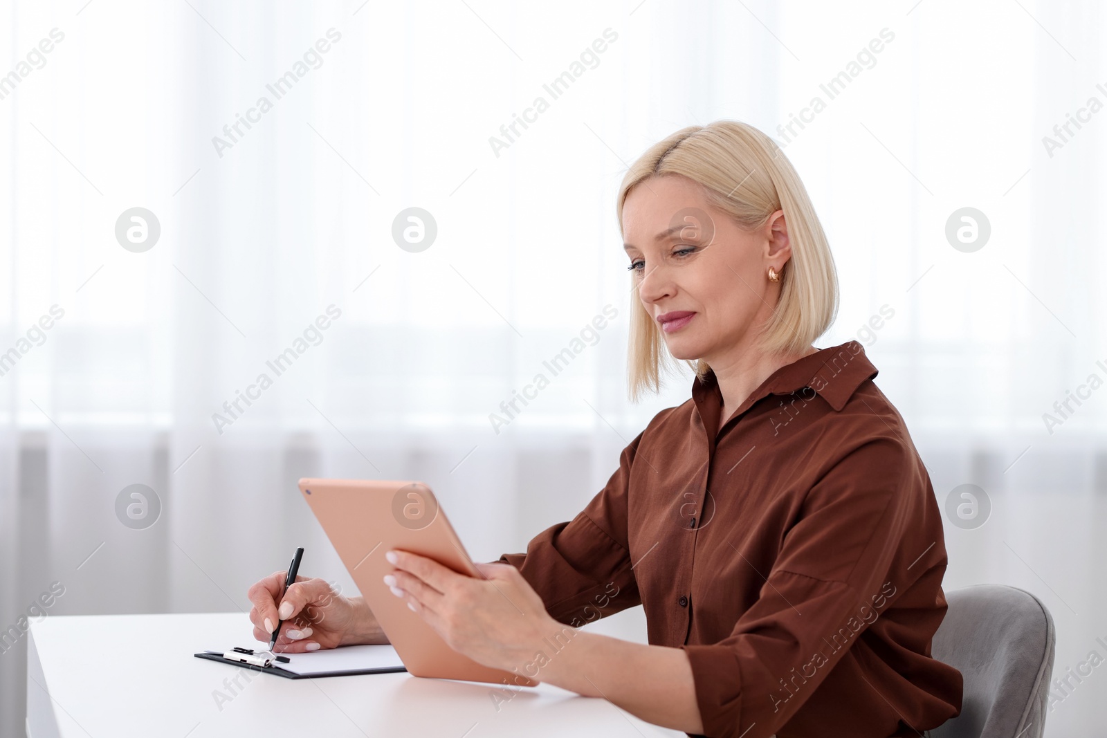 Professional psychologist with tablet taking notes at table in office Photo of Professional psychologist with tablet taking notes at table in office
