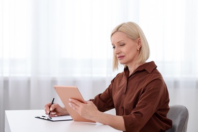 Photo of Professional psychologist with tablet taking notes at table in office
