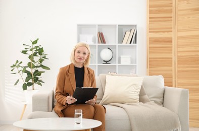 Photo of Professional psychologist with clipboard on sofa in office
