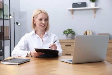 Photo of Professional psychologist taking notes while working with laptop at table in office