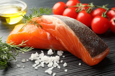 Photo of Seafood. Pieces of salmon fillet, spices, tomatoes and oil on black wooden table, closeup