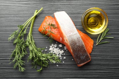 Photo of Seafood. Pieces of salmon fillet, spices and oil on black wooden table, flat lay