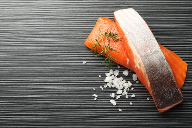 Photo of Seafood. Pieces of salmon fillet and spices on black wooden table, flat lay. Space for text