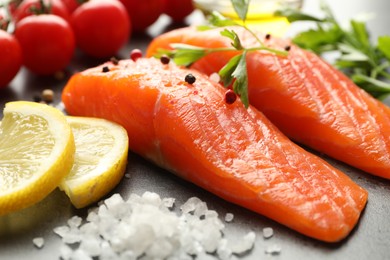 Photo of Seafood. Pieces of salmon fillet, spices, lemon slices and tomatoes on gray table, closeup