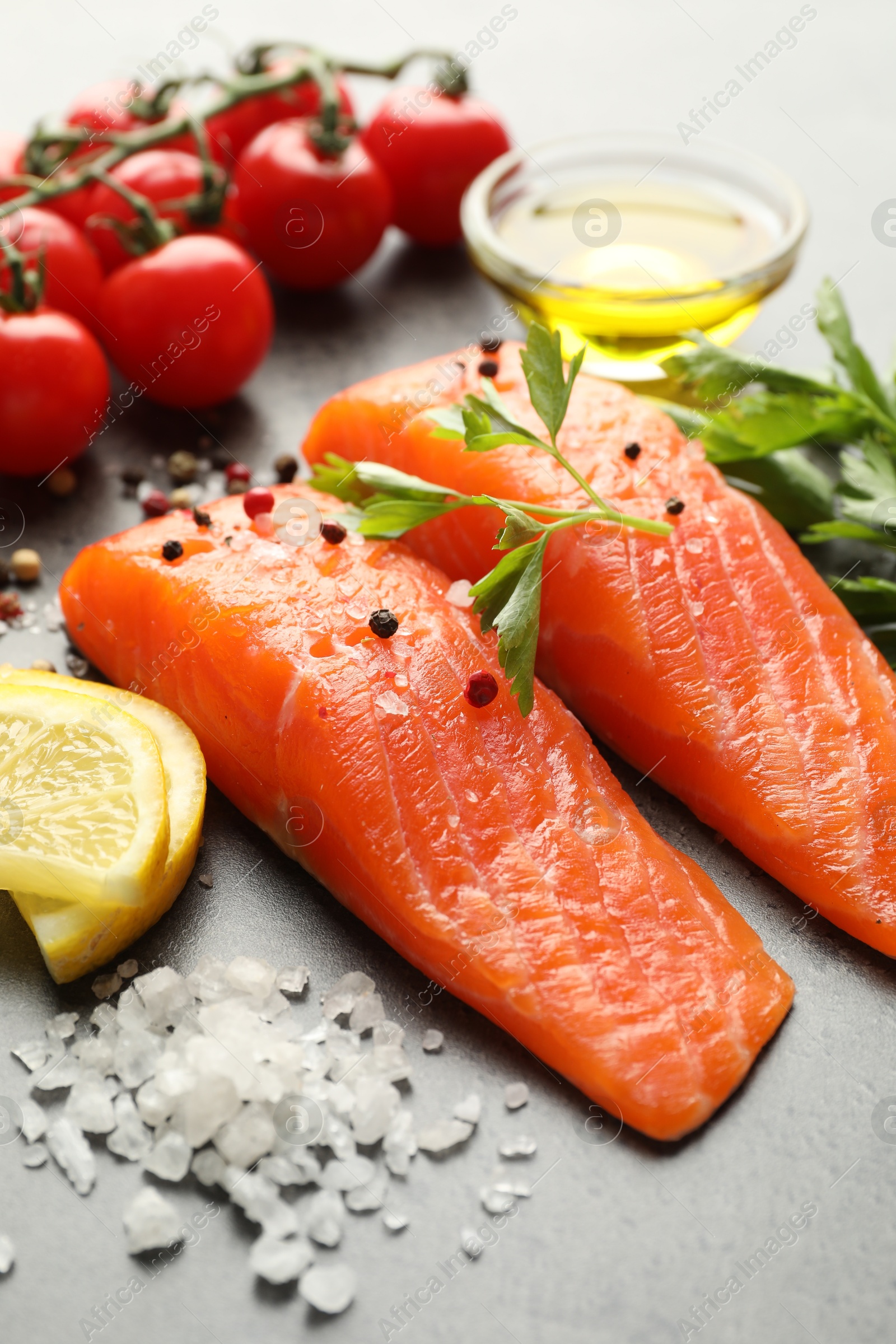 Seafood. Pieces of salmon fillet, tomatoes, lemon slices, oil and spices on gray table, closeup Photo of Seafood. Pieces of salmon fillet, tomatoes, lemon slices, oil and spices on gray table, closeup