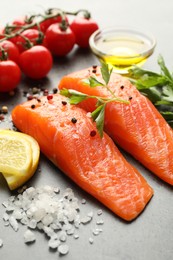 Photo of Seafood. Pieces of salmon fillet, tomatoes, lemon slices, oil and spices on gray table, closeup