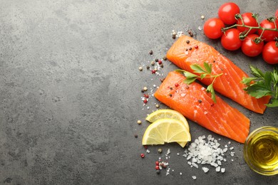 Photo of Seafood. Pieces of salmon fillet, tomatoes, lemon slices, oil and spices on gray textured table, flat lay. Space for text