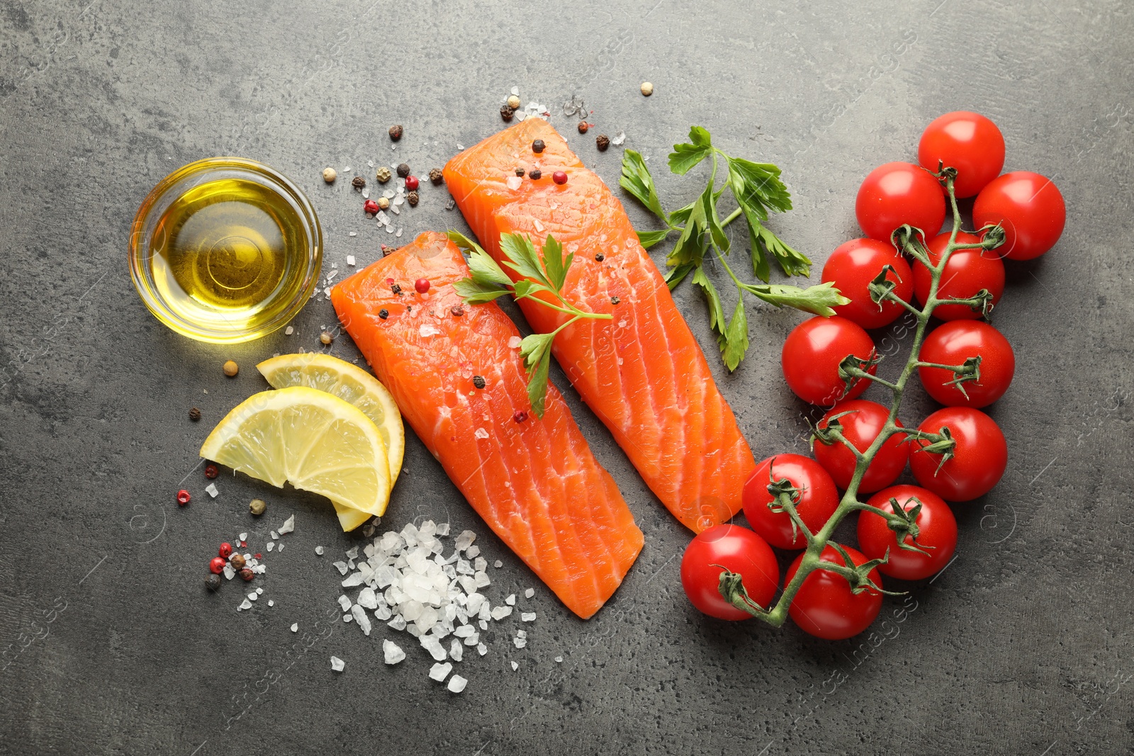 Seafood. Pieces of salmon fillet, tomatoes, lemon slices, oil and spices on gray textured table, flat lay Photo of Seafood. Pieces of salmon fillet, tomatoes, lemon slices, oil and spices on gray textured table, flat lay