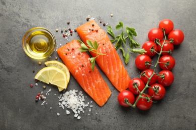 Photo of Seafood. Pieces of salmon fillet, tomatoes, lemon slices, oil and spices on gray textured table, flat lay