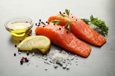 Photo of Seafood. Pieces of salmon fillet, spices, lemon slices and oil on gray table