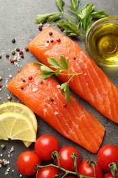 Photo of Seafood. Pieces of salmon fillet, tomatoes, lemon slices, oil and spices on gray table, flat lay