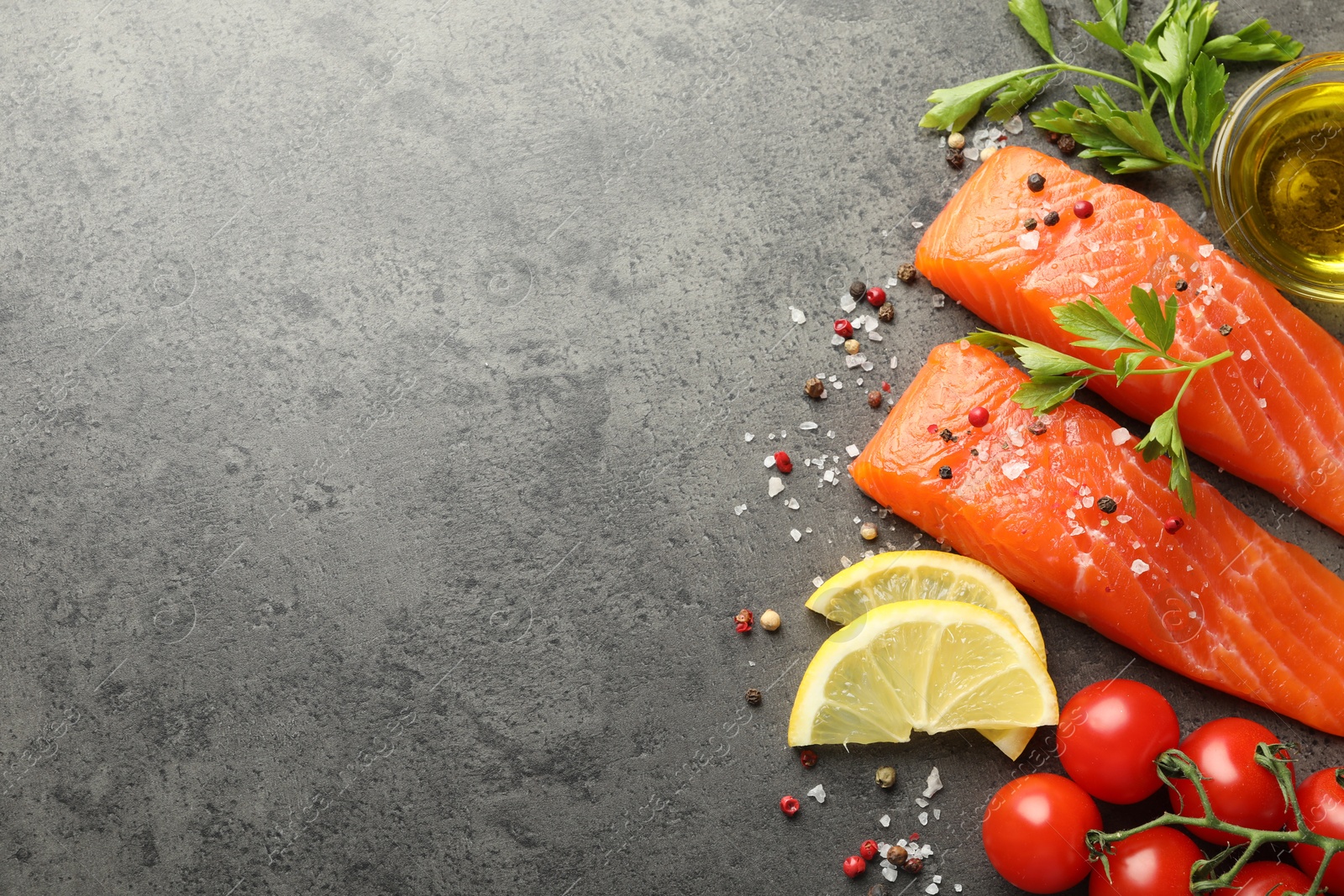 Seafood. Pieces of salmon fillet, tomatoes, lemon slices, oil and spices on gray textured table, flat lay. Space for text Photo of Seafood. Pieces of salmon fillet, tomatoes, lemon slices, oil and spices on gray textured table, flat lay. Space for text