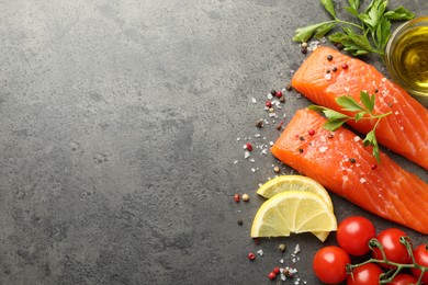 Photo of Seafood. Pieces of salmon fillet, tomatoes, lemon slices, oil and spices on gray textured table, flat lay. Space for text