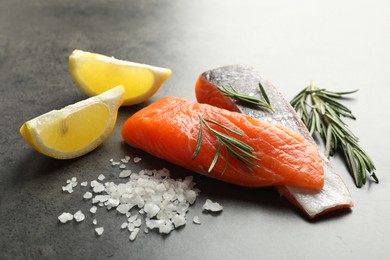 Photo of Seafood. Pieces of salmon fillet, spices and lemon wedges on gray table, closeup