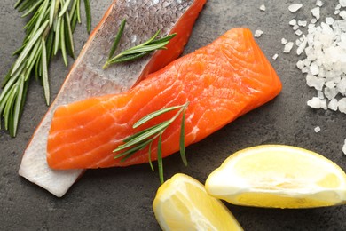 Photo of Seafood. Pieces of salmon fillet, spices and lemon wedges on gray textured table, flat lay