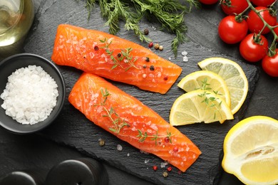 Photo of Seafood. Pieces of salmon fillet, tomatoes, lemon slices and spices on black textured table, flat lay
