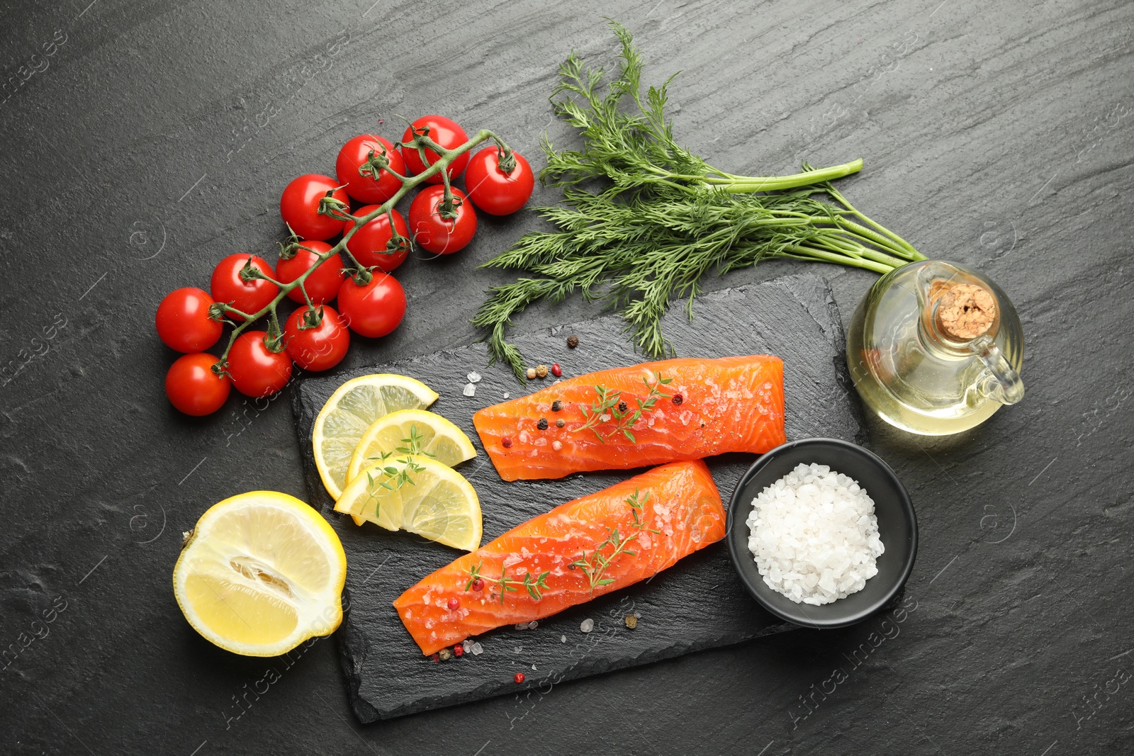 Seafood. Pieces of salmon fillet, tomatoes, lemon slices, oil and spices on black textured table, flat lay Photo of Seafood. Pieces of salmon fillet, tomatoes, lemon slices, oil and spices on black textured table, flat lay