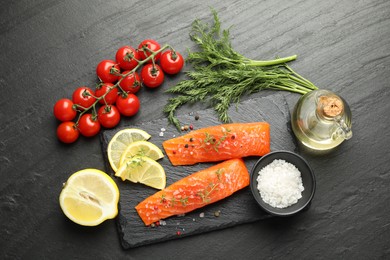 Photo of Seafood. Pieces of salmon fillet, tomatoes, lemon slices, oil and spices on black textured table, flat lay