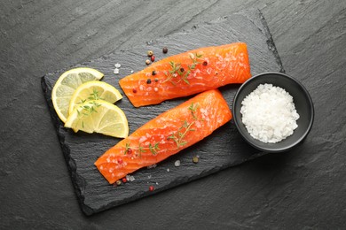 Photo of Seafood. Pieces of salmon fillet with spices and lemon slices on black textured table, flat lay