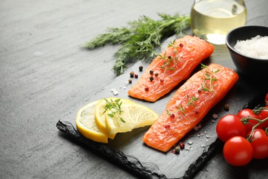 Photo of Seafood. Pieces of salmon fillet, spices, tomatoes, oil and lemon slices on black textured table, closeup