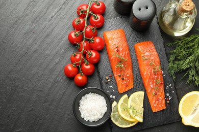 Photo of Seafood. Pieces of salmon fillet, spices, tomatoes, oil and lemon slices on black textured table, flat lay. Space for text