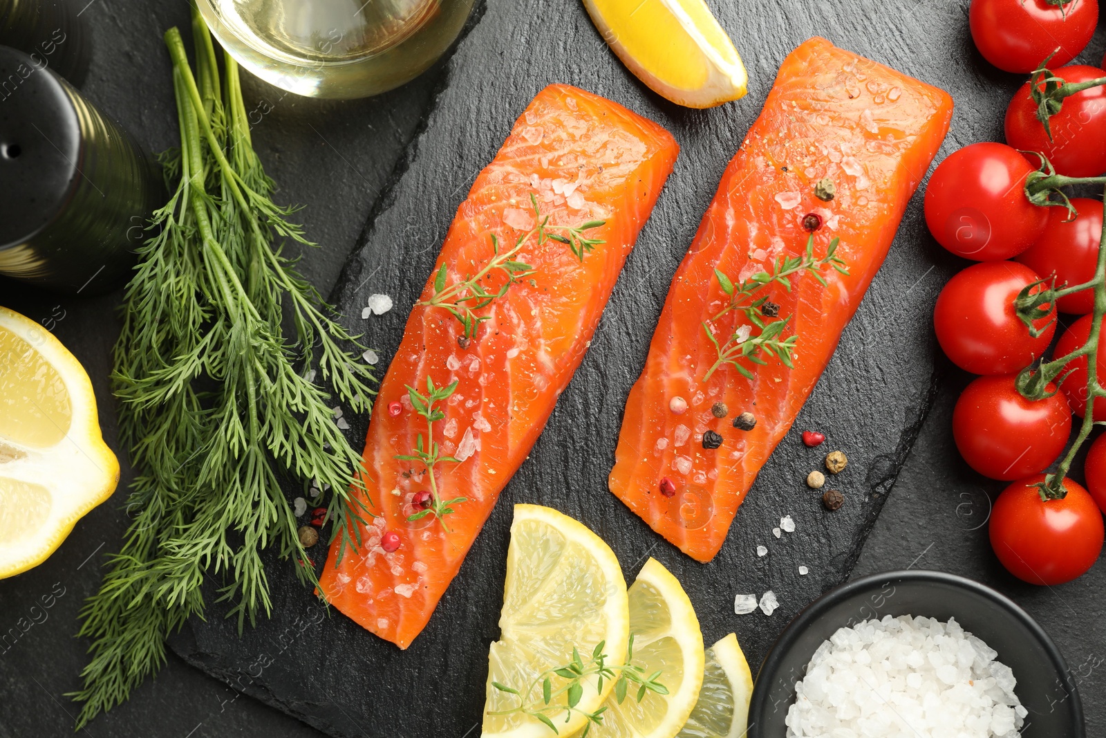 Seafood. Pieces of salmon fillet, spices, tomatoes, oil and lemon slices on black textured table, flat lay Photo of Seafood. Pieces of salmon fillet, spices, tomatoes, oil and lemon slices on black textured table, flat lay