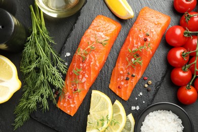 Photo of Seafood. Pieces of salmon fillet, spices, tomatoes, oil and lemon slices on black textured table, flat lay
