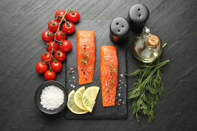 Photo of Seafood. Pieces of salmon fillet, spices, tomatoes, oil and lemon slices on black textured table, flat lay