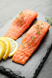 Photo of Seafood. Pieces of salmon fillet, thyme and lemon slices on black table, closeup