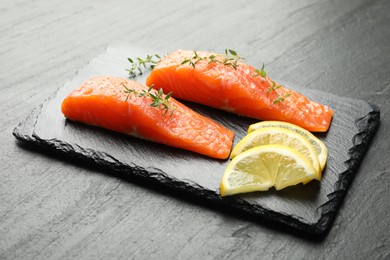 Photo of Seafood. Pieces of salmon fillet, thyme and lemon slices on black textured table, closeup