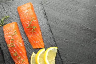 Photo of Seafood. Pieces of salmon fillet, thyme and lemon slices on black textured table, top view. Space for text