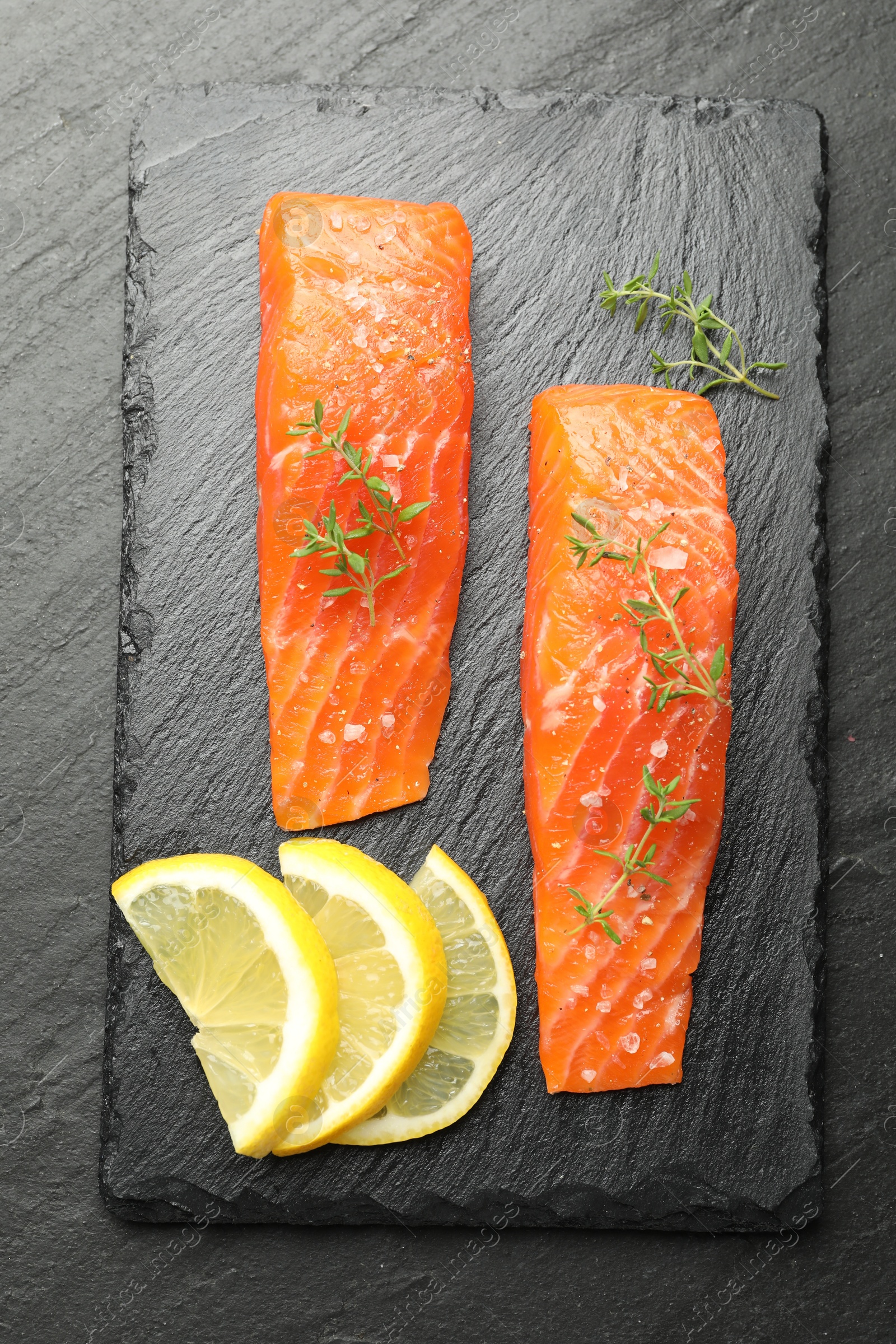 Seafood. Pieces of salmon fillet, thyme and lemon slices on black textured table, top view Photo of Seafood. Pieces of salmon fillet, thyme and lemon slices on black textured table, top view