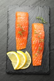 Photo of Seafood. Pieces of salmon fillet, thyme and lemon slices on black textured table, top view