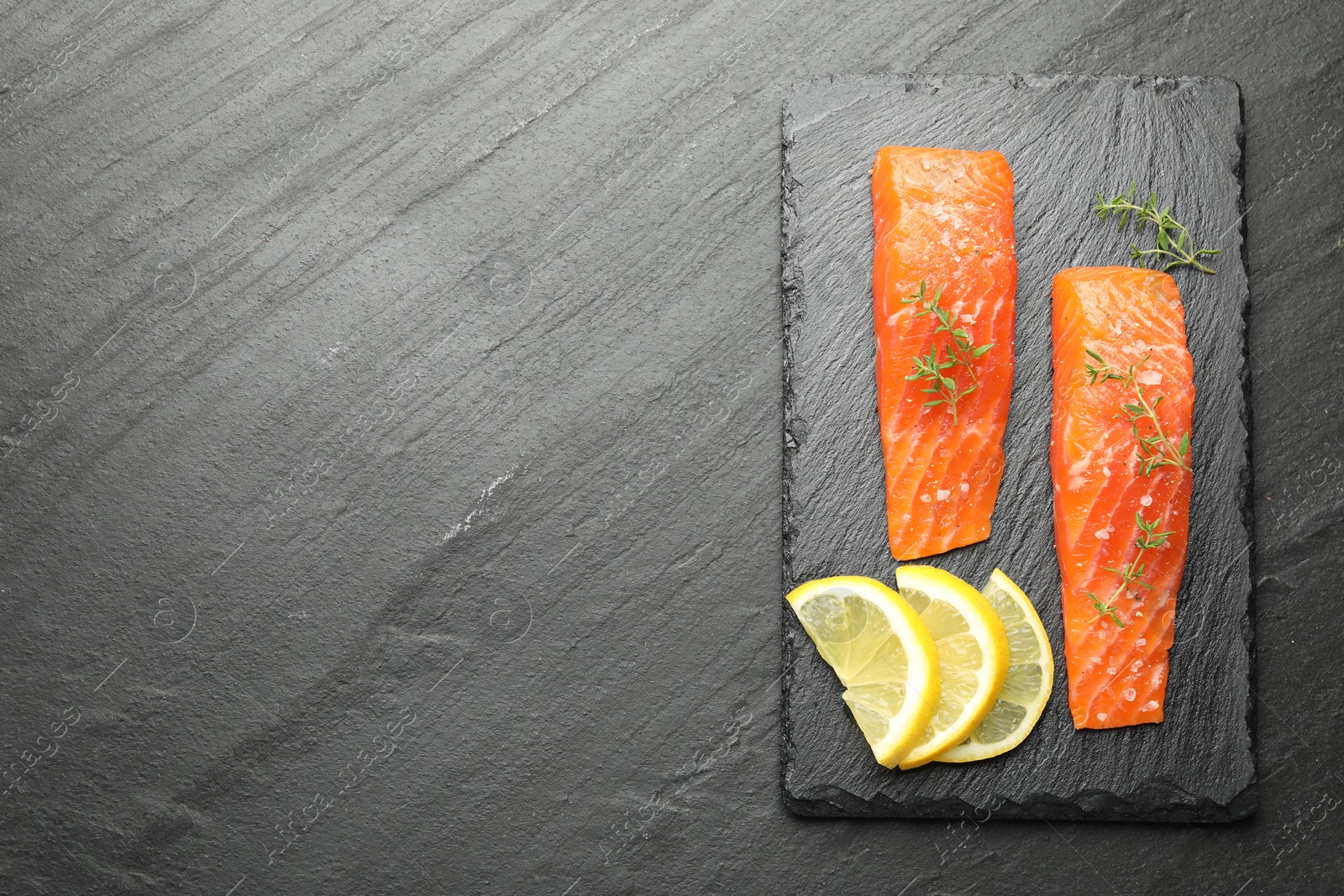 Seafood. Pieces of salmon fillet, thyme and lemon slices on black textured table, top view. Space for text Photo of Seafood. Pieces of salmon fillet, thyme and lemon slices on black textured table, top view. Space for text